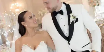 A bride and groom posing together in a luxurious ballroom with a large chandelier.
