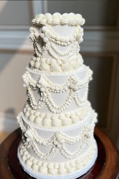 A tall, multi-tiered white wedding cake decorated with elaborate piped frosting and pearl accents.