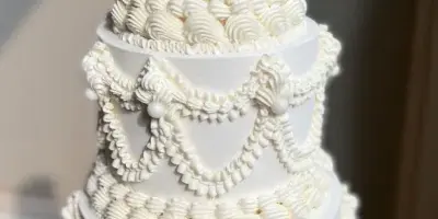 A tall, multi-tiered white wedding cake decorated with elaborate piped frosting and pearl accents.
