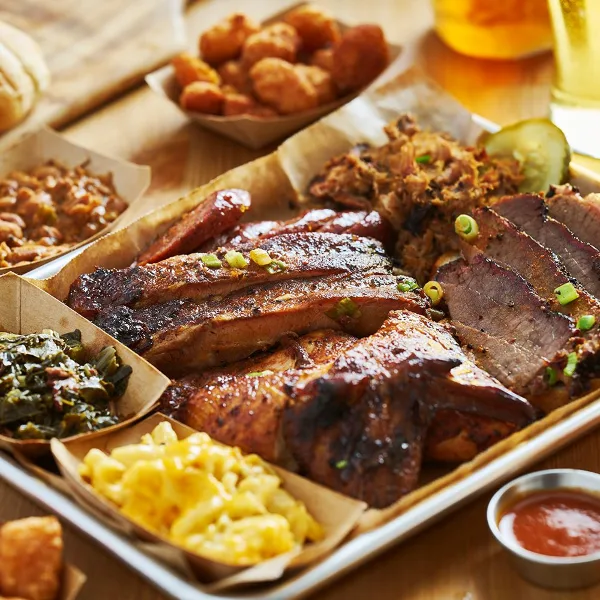 A large BBQ platter featuring smoked brisket, ribs, pulled pork, and sides like mac and cheese and collard greens.