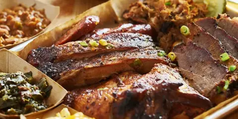 A large BBQ platter featuring smoked brisket, ribs, pulled pork, and sides like mac and cheese and collard greens.