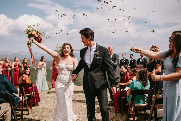 A bride and groom walking down an outdoor aisle with guests and wedding party members on either side.