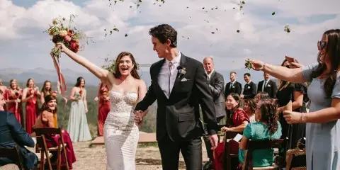 A bride and groom walking down an outdoor aisle with guests and wedding party members on either side.
