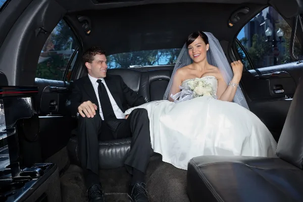 A bride and groom sitting in the back seat of a luxury car.
