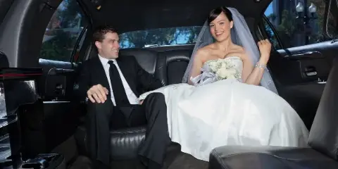 A bride and groom sitting in the back seat of a luxury car.