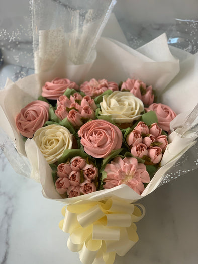 A wrapped bouquet of pink and white buttercream cupcakes styled to look like flowers, tied with a yellow ribbon.