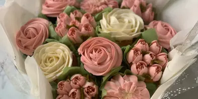 A wrapped bouquet of pink and white buttercream cupcakes styled to look like flowers, tied with a yellow ribbon.