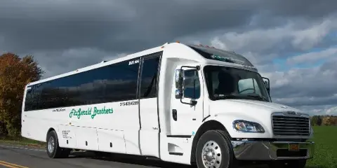 A white FitzGerald Brothers charter bus driving on a road under a cloudy sky.