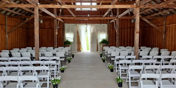 Interior view of a barn wedding venue with rows of white chairs and floral decorations.