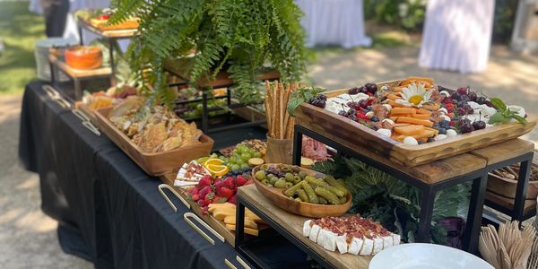Outdoor catering buffet featuring a charcuterie board, fruit platters, and other food items on a table.