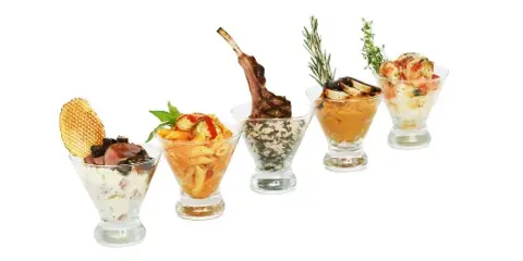 A row of five gourmet appetizers served in glass cups, featuring various dishes including pasta, a lamb chop, and shrimp.