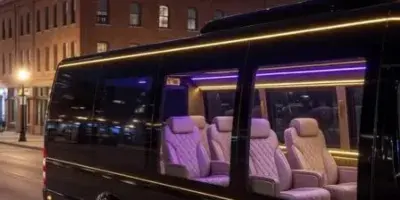Black party bus with illuminated interior seating and exterior LED lighting parked on a city street at night