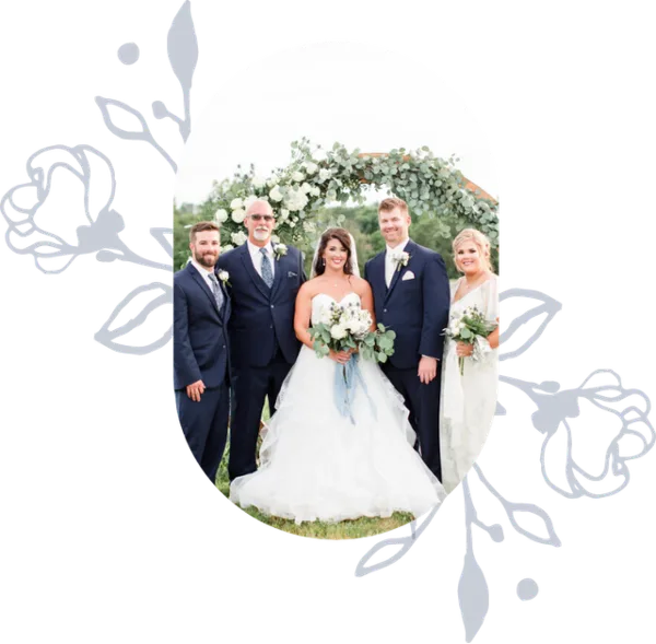 A wedding party posing in front of a floral arbor at an outdoor wedding venue.
