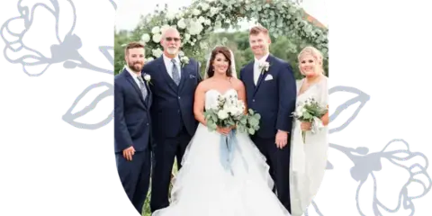 A wedding party posing in front of a floral arbor at an outdoor wedding venue.