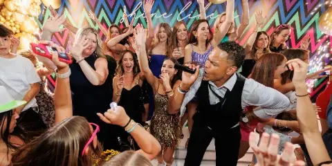A performer with a microphone interacting with a cheering crowd at a decorated event venue.