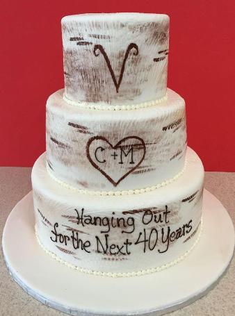 A three-tiered white cake with rustic brown brushstroke detailing, a heart design, and the text 'Hanging Out for the Next 40 Years'.