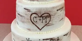 A three-tiered white cake with rustic brown brushstroke detailing, a heart design, and the text 'Hanging Out for the Next 40 Years'.