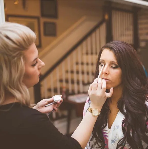 A makeup artist applying makeup to a seated client in an indoor setting.