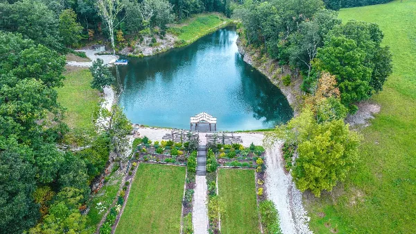 Aerial view of a rustic wedding venue featuring a pond, landscaped gardens, and a covered ceremony pavilion.