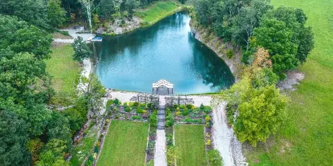Aerial view of a rustic wedding venue featuring a pond, landscaped gardens, and a covered ceremony pavilion.