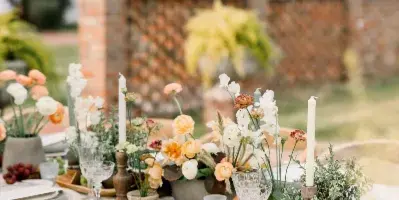 A close-up of an elegantly set wedding table featuring floral centerpieces, tall white candles, and fine dining ware.