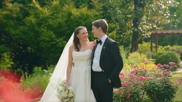 A bride and groom standing together in a garden, looking at each other affectionately.