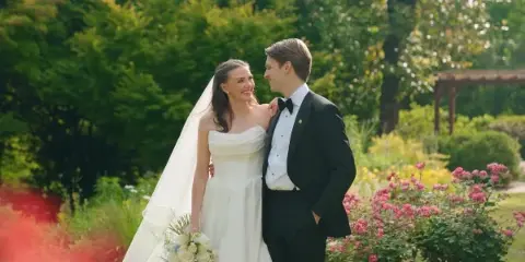 A bride and groom standing together in a garden, looking at each other affectionately.