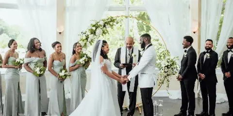A wedding ceremony with a bride and groom exchanging vows under a floral arch, surrounded by bridesmaids and groomsmen.