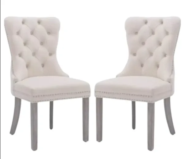 A pair of white upholstered dining chairs with tufted backs and wooden legs.
