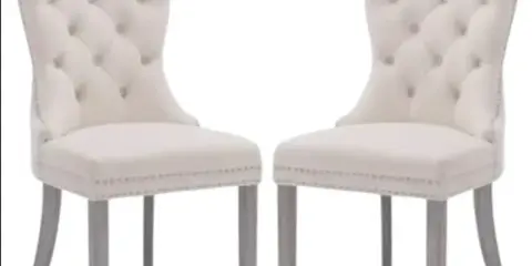 A pair of white upholstered dining chairs with tufted backs and wooden legs.