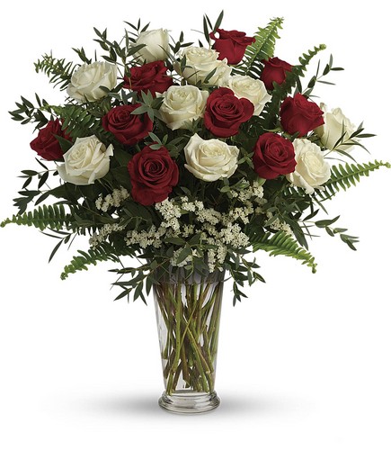 A vase filled with red and white roses and greenery.
