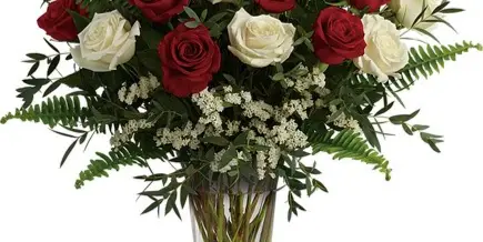 A vase filled with red and white roses and greenery.