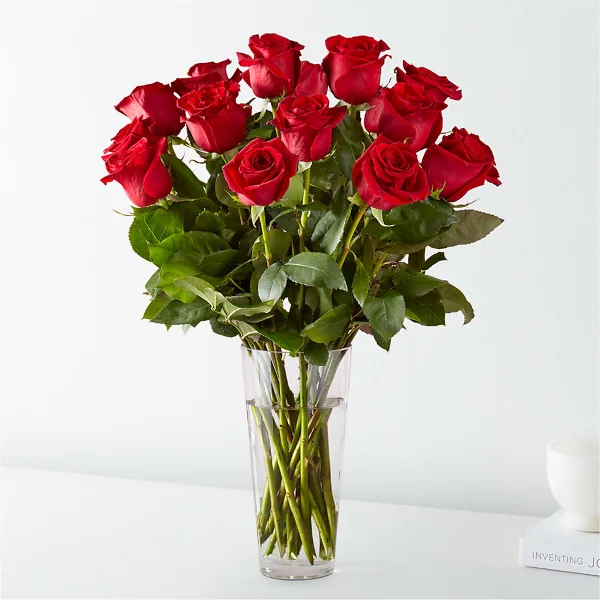 A bouquet of long-stem red roses arranged in a clear glass vase.