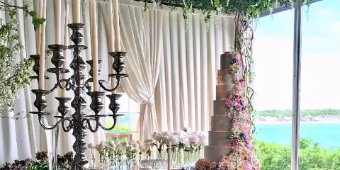 A tall, multi-tiered wedding cake decorated with cascading pink and white flowers, displayed on a table next to a large silver candelabra and floral arrangements.