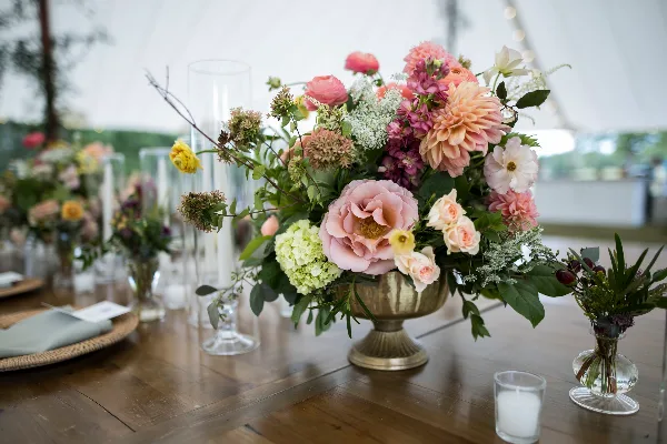 A lush floral centerpiece featuring pink and white blooms in a brass vase on a wooden table.