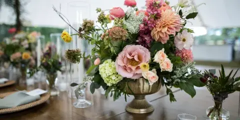A lush floral centerpiece featuring pink and white blooms in a brass vase on a wooden table.