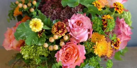 A vibrant floral arrangement in a glass vase featuring pink and orange roses, dahlias, and greenery.