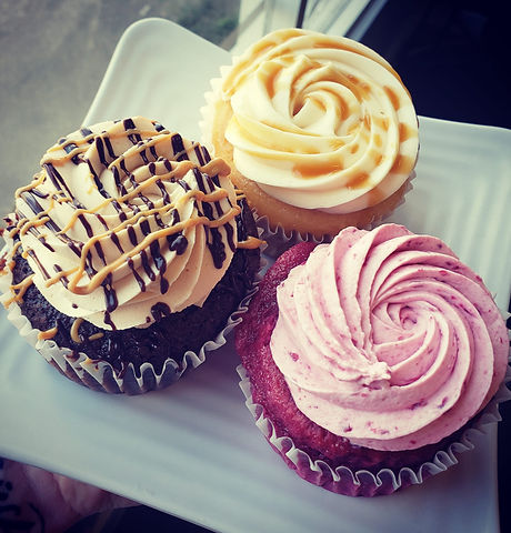 Three decorated cupcakes with different frosting colors and toppings on a white plate