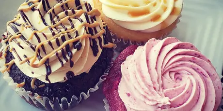 Three decorated cupcakes with different frosting colors and toppings on a white plate