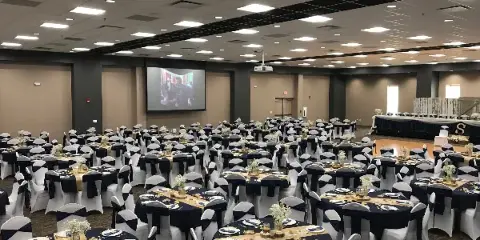 A large banquet hall set up for a wedding reception with round tables, white chair covers, and a head table.