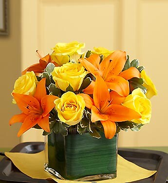 A floral arrangement consisting of yellow roses and orange lilies in a green vase.