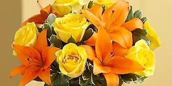 A floral arrangement consisting of yellow roses and orange lilies in a green vase.