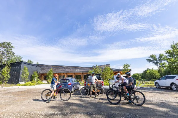 Exterior view of the New England Outdoor Center resort building with guests and mountain bikes in the parking lot.