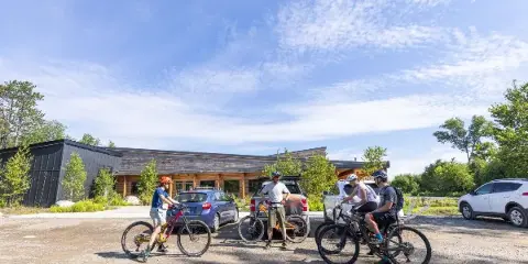 Exterior view of the New England Outdoor Center resort building with guests and mountain bikes in the parking lot.