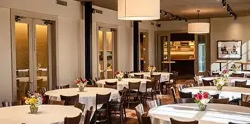 A private event venue with round tables set for a dinner, featuring white tablecloths and floral centerpieces.