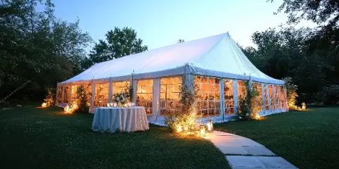 A large white event tent set up on a grassy lawn at dusk, featuring a decorated table and string lights.