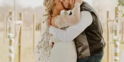 A bride and groom sharing a kiss under a floral arch during an outdoor wedding ceremony in a vineyard.