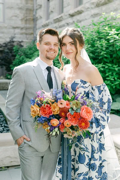A bride and groom standing together outdoors, with the bride holding a large, colorful bouquet of flowers.