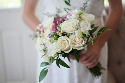 A bride holding a bouquet of white roses and greenery.