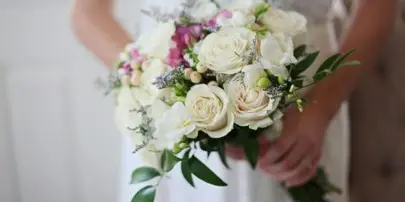 A bride holding a bouquet of white roses and greenery.